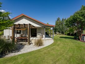 A backyard with a covered patio, wooden pergola, outdoor furniture, green lawn, and trees at Lake Hawea Hideaway - Lake Hawea Holiday Home