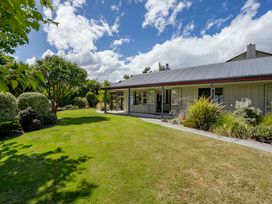 A lawn with shrubs and trees next to a house with a covered porch at Lake Hawea Hideaway Lake Hawea