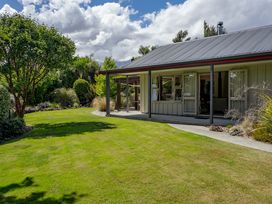 A garden with grass and trees next to a house with a covered porch at Lake Hawea Hideaway Lake Hawea