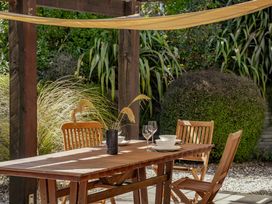 An outdoor wooden table with chairs under a wooden pergola surrounded by plants at Lake Hawea Hideaway Lake Hawea