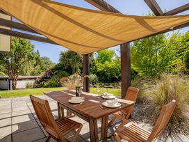 An outdoor patio with a wooden table set for four under a fabric shade with greenery and garden plants in the background at Lake Hawea Hideaway Lake Hawea