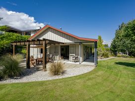 An outdoor patio with wooden pergola and seating area beside a single-story house with lawn and trees at Lake Hawea Hideaway Lake Hawea