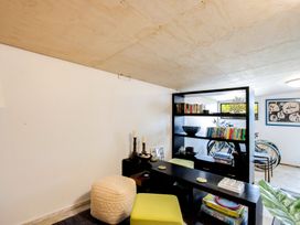 A room with a black bookshelf containing books and decorative items two green stools a beige cushion and bicycles in the background at Bird and Fish - Napier Holiday Home in Napier