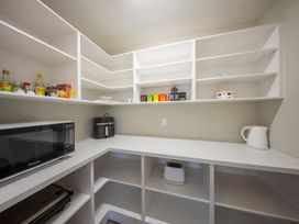 A pantry with shelves, a microwave, kettle, and various items at Fiordland Getaway - Te Anau Holiday Home, Fiordland