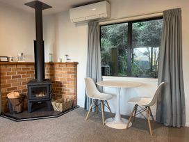 A living room with a wood stove and round table at Bushside Cottage - Akaroa