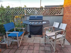 A barbecue grill and two chairs on a patio at Riviera Casa - Mount Maunganui Holiday Home Mount Maunganui