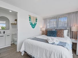 A bedroom with a bed, bedside tables, and an adjacent bathroom at Sun Kissed Pool Villa - Mangawhai Heads