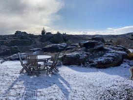 A wooden table with six chairs on snowy ground near rocky terrain under a partly cloudy sky at A Place in Thyme - Alexandra Holiday Home in Alexandra