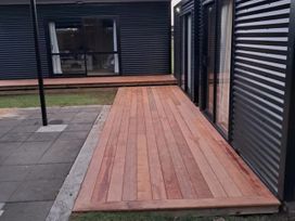 An outdoor area with wooden decking and glass doors at The Bach at 44 - Cooks Beach