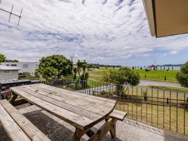 An outdoor area with a table and chairs overlooking the grass and water at Te Tiriti Beach House in Paihia