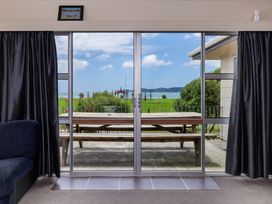 A view from a living room showing a sliding door opening to a patio with a table and grass at Te Tiriti Beach House - Paihia