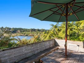 An outdoor wooden seating area with a table and a green umbrella overlooking a lake surrounded by trees at Okere Retreat - Lake Rotoiti Getaway