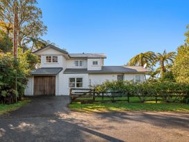 A white two-story house with a garage next to the driveway and a wooden fence surrounded by trees at Okere Retreat - Lake Rotoiti Getaway