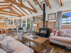 A living room with wooden beams a wood stove three sofas a wooden coffee table and a dining table with chairs at Okere Retreat - Lake Rotoiti Getaway in Lake Rotoiti