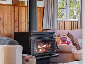 A wood burning stove with a fire inside next to a sofa with patterned cushions in a room with wood paneling and a window showing greenery at Okere Retreat - Lake Rotoiti Getaway Lake Rotoiti