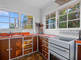 A kitchen with wooden cabinets orange countertops a white stove and large windows showing trees outside at Okere Retreat - Lake Rotoiti Getaway Lake Rotoiti