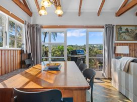 A dining room with a wooden table surrounded by chairs and a bowl on the table next to a living area with a sofa and lamp beside a window and glass doors leading to an outdoor space with a barbecue grill at Okere Retreat - Lake Rotoiti Getaway