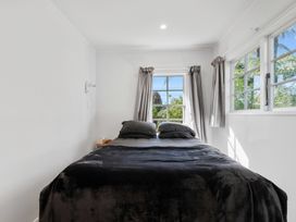 A bedroom with a bed covered in dark bedding and two pillows next to windows with curtains at Okere Retreat - Lake Rotoiti Getaway Lake Rotoiti