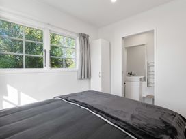 A bedroom with a bed facing windows a white wardrobe and an open door leading to a bathroom at Okere Retreat - Lake Rotoiti Getaway
