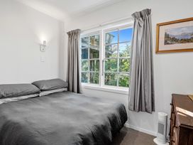 A bedroom with a bed gray bedding a window with gray curtains a wooden dresser and a heater at Okere Retreat - Lake Rotoiti Getaway in Lake Rotoiti