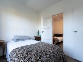 A bedroom with a bed covered by a leopard print blanket and a bedside table next to an open door showing another room with a bed at Okere Retreat - Lake Rotoiti Getaway Lake Rotoiti