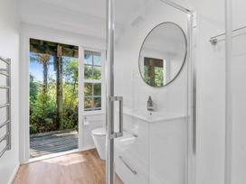 A bathroom with a white vanity and round mirror and a door leading to an outdoor deck at Okere Retreat - Lake Rotoiti Getaway