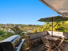 An outdoor wooden deck with a table and chairs under an umbrella and a barbecue grill overlooking trees and a lake at Okere Retreat - Lake Rotoiti Getaway