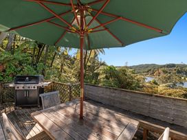 An outdoor wooden deck with a table and chairs under a large green umbrella a barbecue grill and trees surrounding the area with a lake and hills in the background at Okere Retreat - Lake Rotoiti Getaway Lake Rotoiti