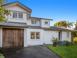 A white two-story house with a wooden garage door and a paved driveway surrounded by grass at Okere Retreat - Lake Rotoiti Getaway in Lake Rotoiti