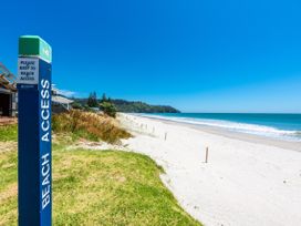 A beach access path with sandy shore and ocean on the right and houses and greenery on the left at The Wallnutt Nook - Waihi Beach