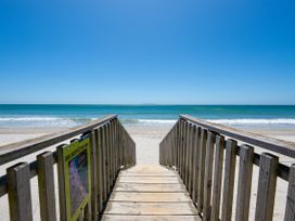 A wooden boardwalk leading to a sandy beach and ocean at The Wallnutt Nook - Waihi Beach