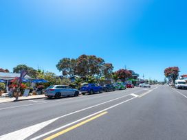 A street with parked cars on both sides and shops with trees along the road at The Wallnutt Nook - Waihi Beach