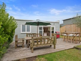 An outdoor wooden deck with a dining table set under a green umbrella and a bar table with stools next to a house at The Wallnutt Nook - Waihi Beach