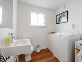 A laundry room with a sink toilet washing machine and wooden floor at The Wallnutt Nook - Waihi Beach