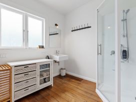 A bathroom with a shower, a white sink, wooden floor, a cabinet with towels and a mirror at The Wallnutt Nook - Waihi Beach Holiday Home in Waihi Beach