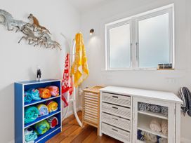 A room with a blue shelf holding rolled towels hooks with hanging towels a wooden laundry basket and a white cabinet with more towels at The Wallnutt Nook - Waihi Beach Holiday Home in Waihi Beach