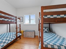 A bedroom with two wooden bunk beds blue and white checkered bedding a window and a storage chest at The Wallnutt Nook - Waihi Beach Holiday Home in Waihi Beach
