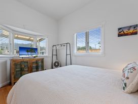 A bedroom with a bed a wooden cabinet with a TV a clothes rack and windows with blinds at The Wallnutt Nook - Waihi Beach Holiday Home in Waihi Beach