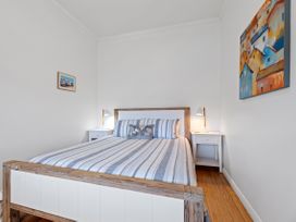 A bedroom with a wooden bed with striped bedding and two bedside tables with lamps at The Wallnutt Nook Waihi Beach