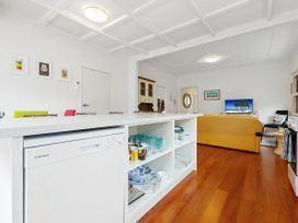A kitchen island with dishes and mugs and a dishwasher in a living room with a yellow couch and TV at The Wallnutt Nook - Waihi Beach