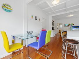 A dining area with colorful chairs around a glass table and a kitchen bar with stools at The Wallnutt Nook - Waihi Beach