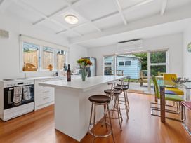 A kitchen with a white island, stools, dining table with colorful chairs and sliding glass doors at The Wallnutt Nook Waihi Beach