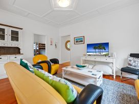 A living room with yellow and black armchairs a yellow sofa a white cabinet a coffee table and a TV on a white TV stand at The Wallnutt Nook Waihi Beach