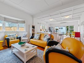 A living room with yellow and black armchairs and sofa with floral pillows by a white coffee table and windows at The Wallnutt Nook - Waihi Beach Holiday Home in Waihi Beach