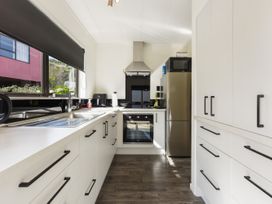 A kitchen with white cabinets black handles a sink oven a refrigerator and a microwave at Tahunanui Shoreside - Nelson Holiday Home in Tahunanui Beach