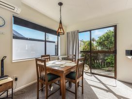 A dining area with a wooden table and four chairs near large windows and a glass door at Tahunanui Shoreside - Nelson Holiday Home in Tahunanui Beach