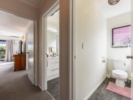 Hallway with open doors showing a bathroom with sink and a separate toilet room and a bedroom with a dresser and television at Tahunanui Shoreside - Nelson Holiday Home in Tahunanui Beach