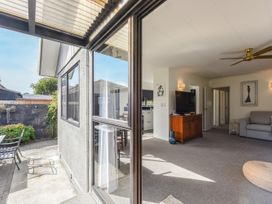 An open sliding glass door showing a living room with a television on a wooden cabinet a gray sofa and outdoor patio furniture at Tahunanui Shoreside - Nelson Holiday Home in Tahunanui Beach