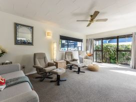 A living room with two armchairs and footrests a patterned chair a sofa and glass doors opening to a garden at Tahunanui Shoreside - Nelson Holiday Home Tahunanui Beach