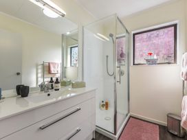 A bathroom with a sink, mirror, shower, pink towels, and a pink rug at Tahunanui Shoreside - Nelson Holiday Home in Tahunanui Beach